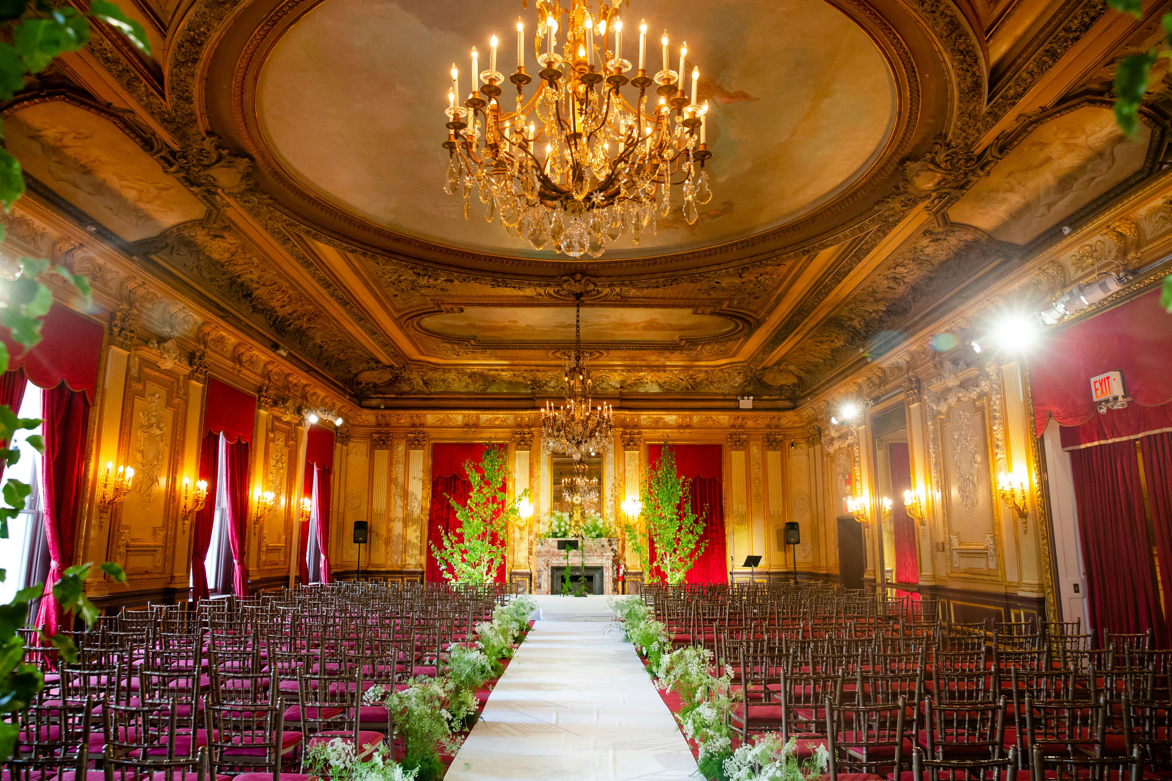 Red and gold wedding ceremony set in an elegant classic theater style venue | PartySlate