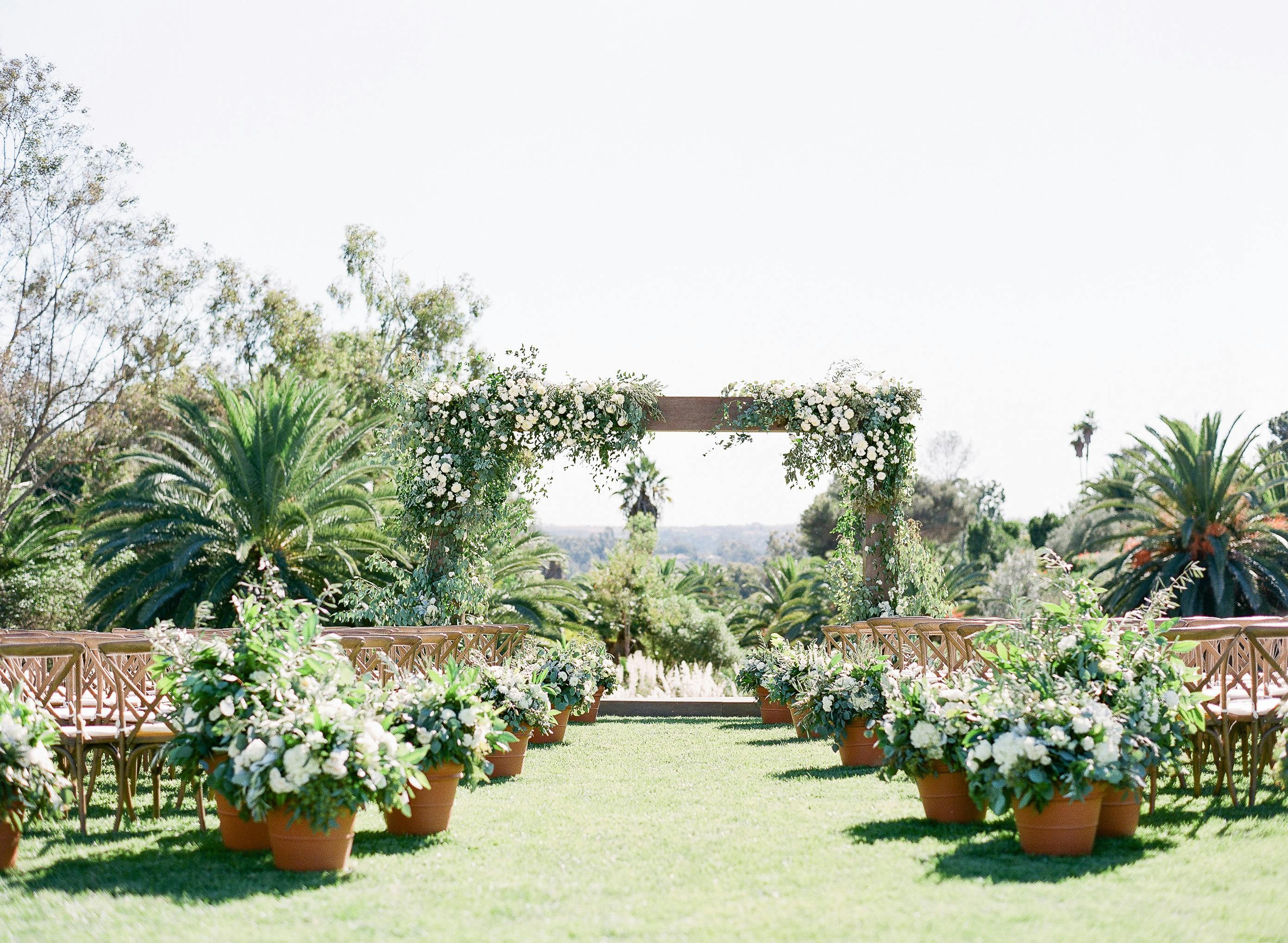Outdoor wedding aisle with potted plants and natural greenery.