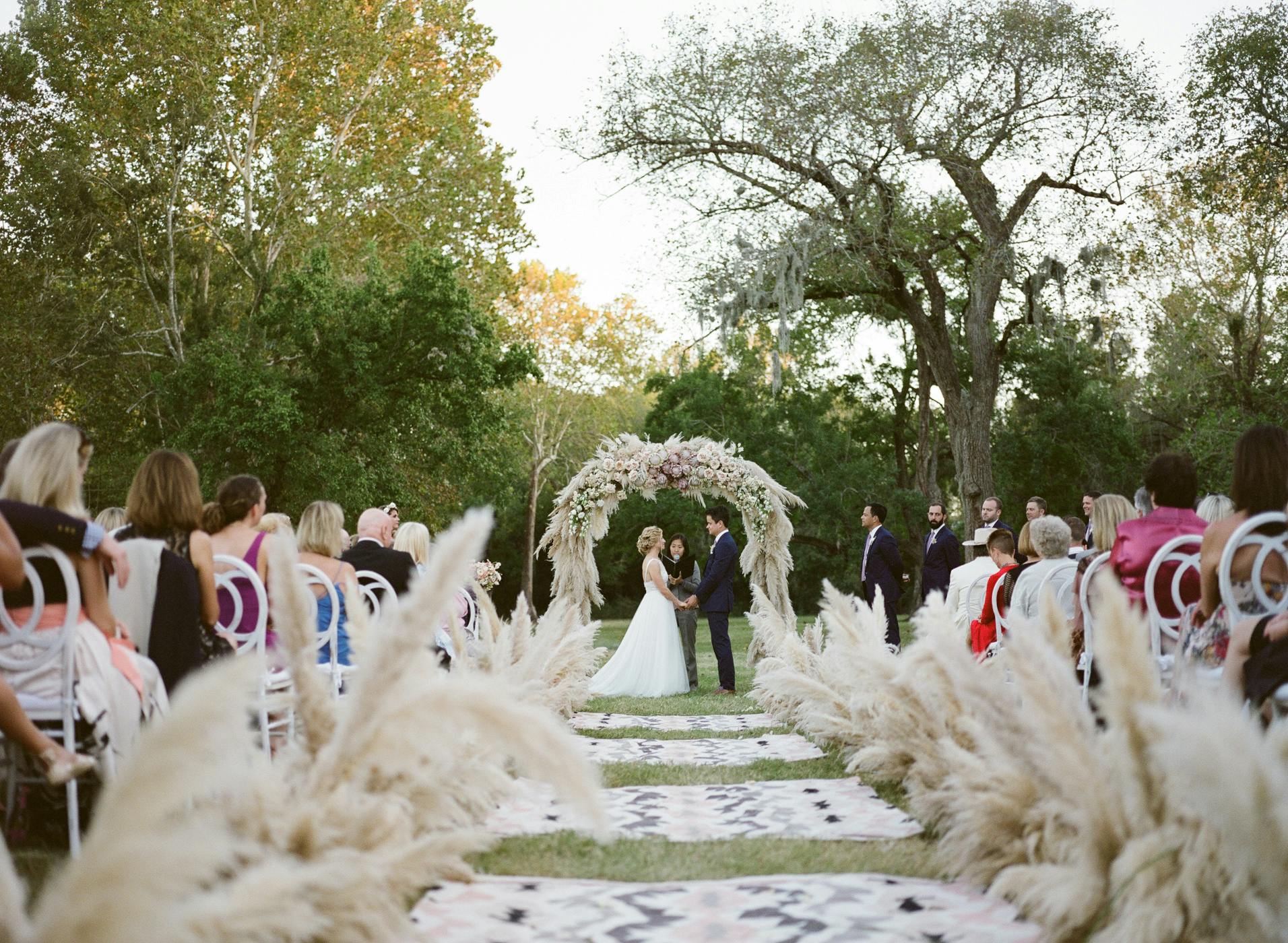 Rustic outdoor wedding with pampas grass and a wedding aisle covered in boho throw rugs | PartySlate