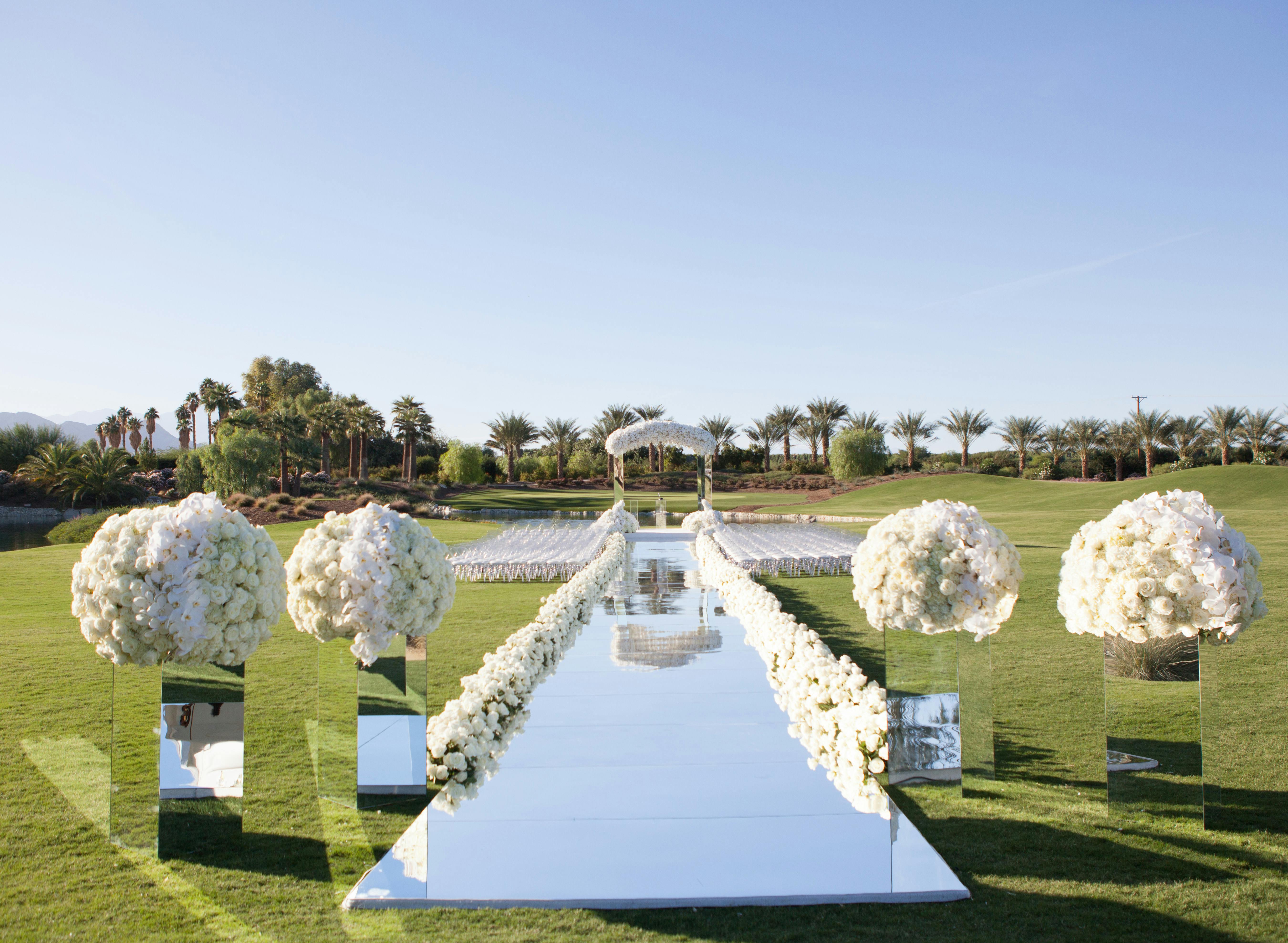 Mirrored wedding aisle with white flowers on mirrored bases in a grassy field | PartySlate