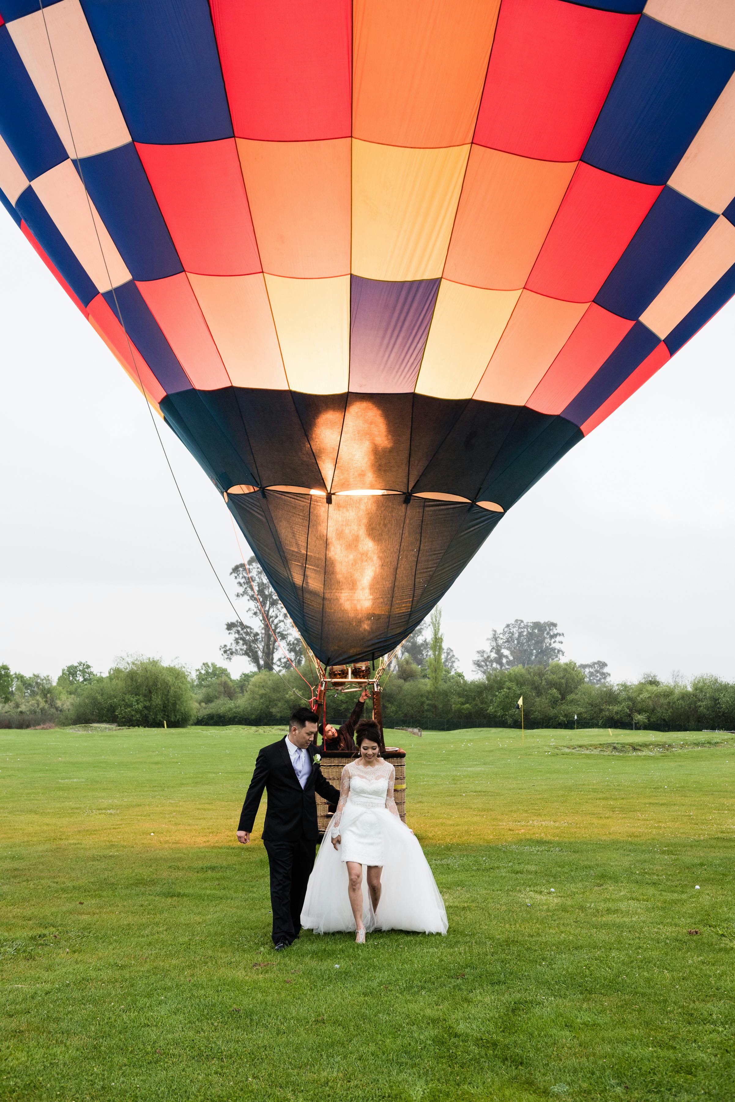 Bride And Groom Stand For Photo-Op Near Hot Air Ballon At Vineyard Wedding in Napa Valley, California | PartySlate