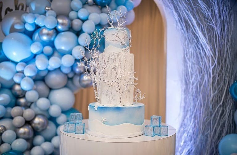Blue and gray balloon installation and an icy blue tiered cake | PartySlate