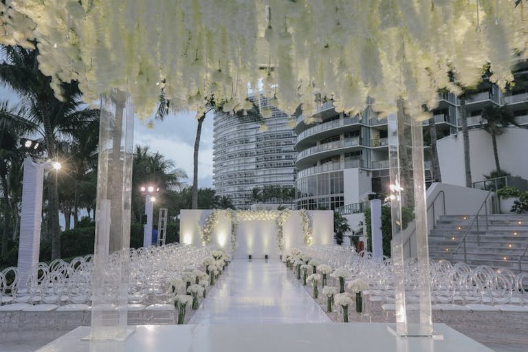 Glass archways at the end of a wedding aisle with white florals overhead | PartySlate