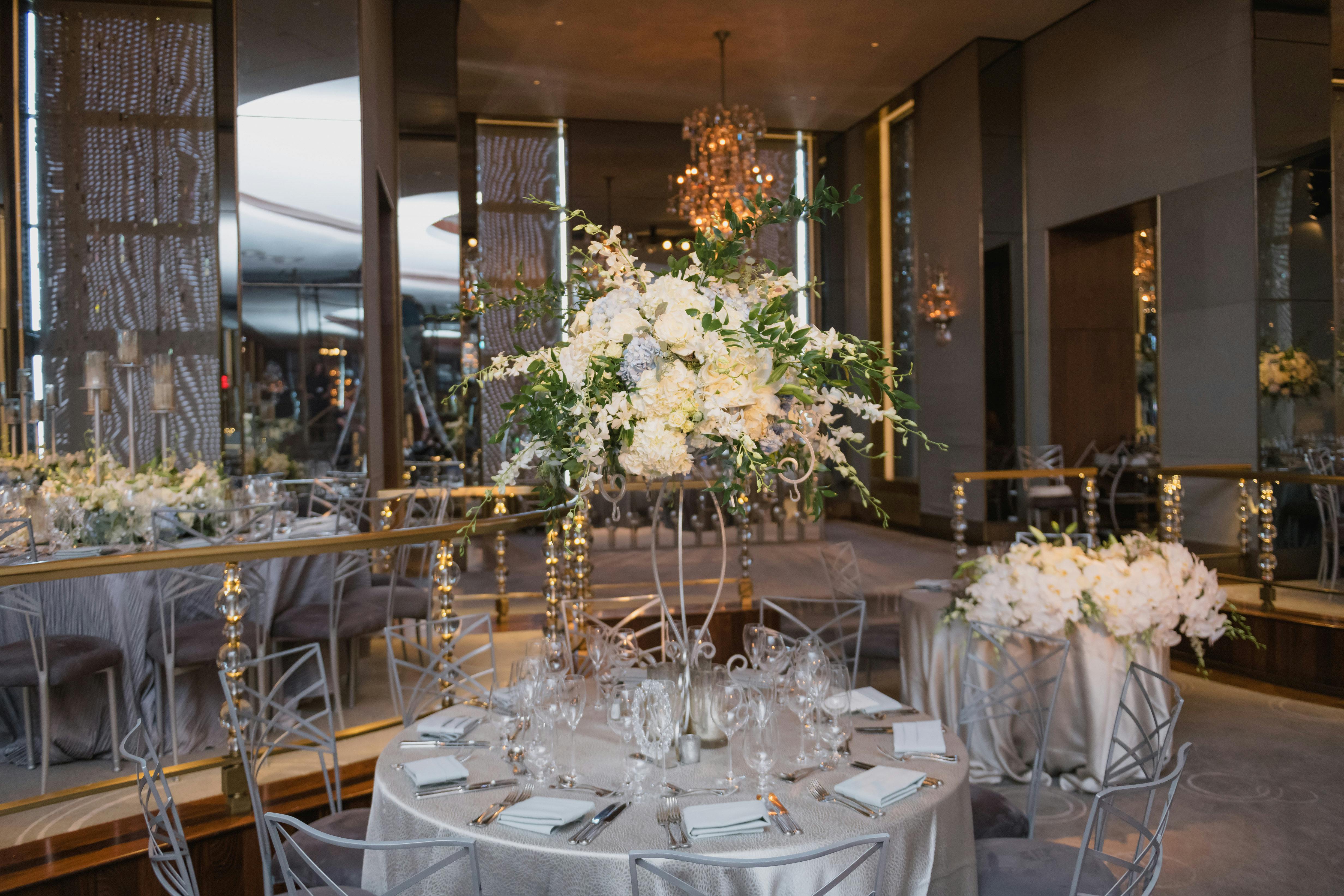 Wedding Reception Venue with a Round Banquet Table Featuring Silver Linen and a Free-Form Wedding Centerpiece of White Hydrangeas and Greens