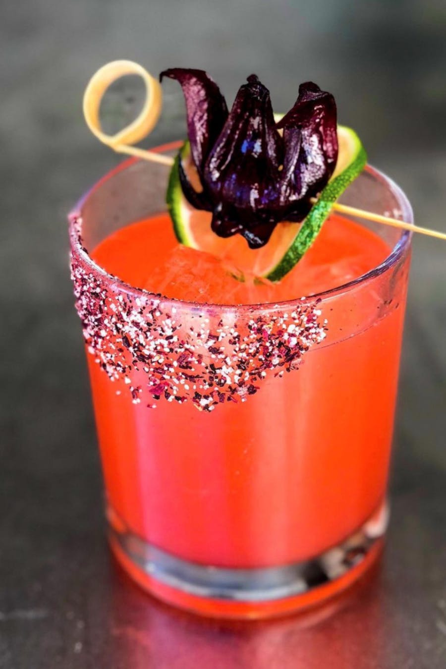 Reddish-Orange Cocktail by Wolfgang Puck Catering With Dried Hibiscus and Cucumber Garnish | PartySlate