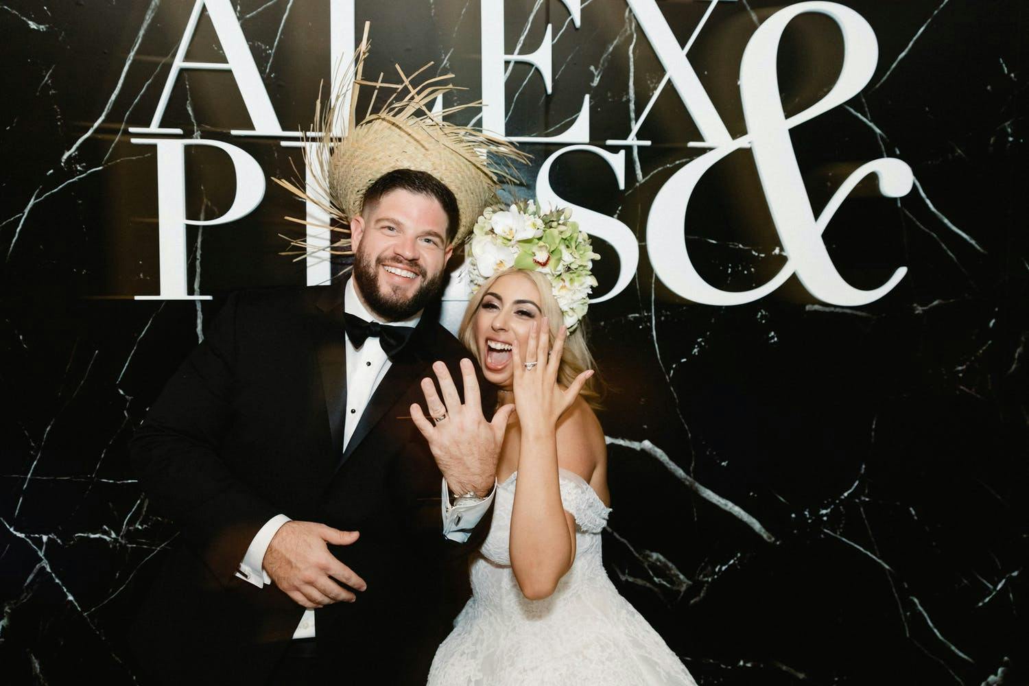 Bride and Groom Show Off Rings in Front of Marbled Black and White Backdrop With Their Names | PartySlate