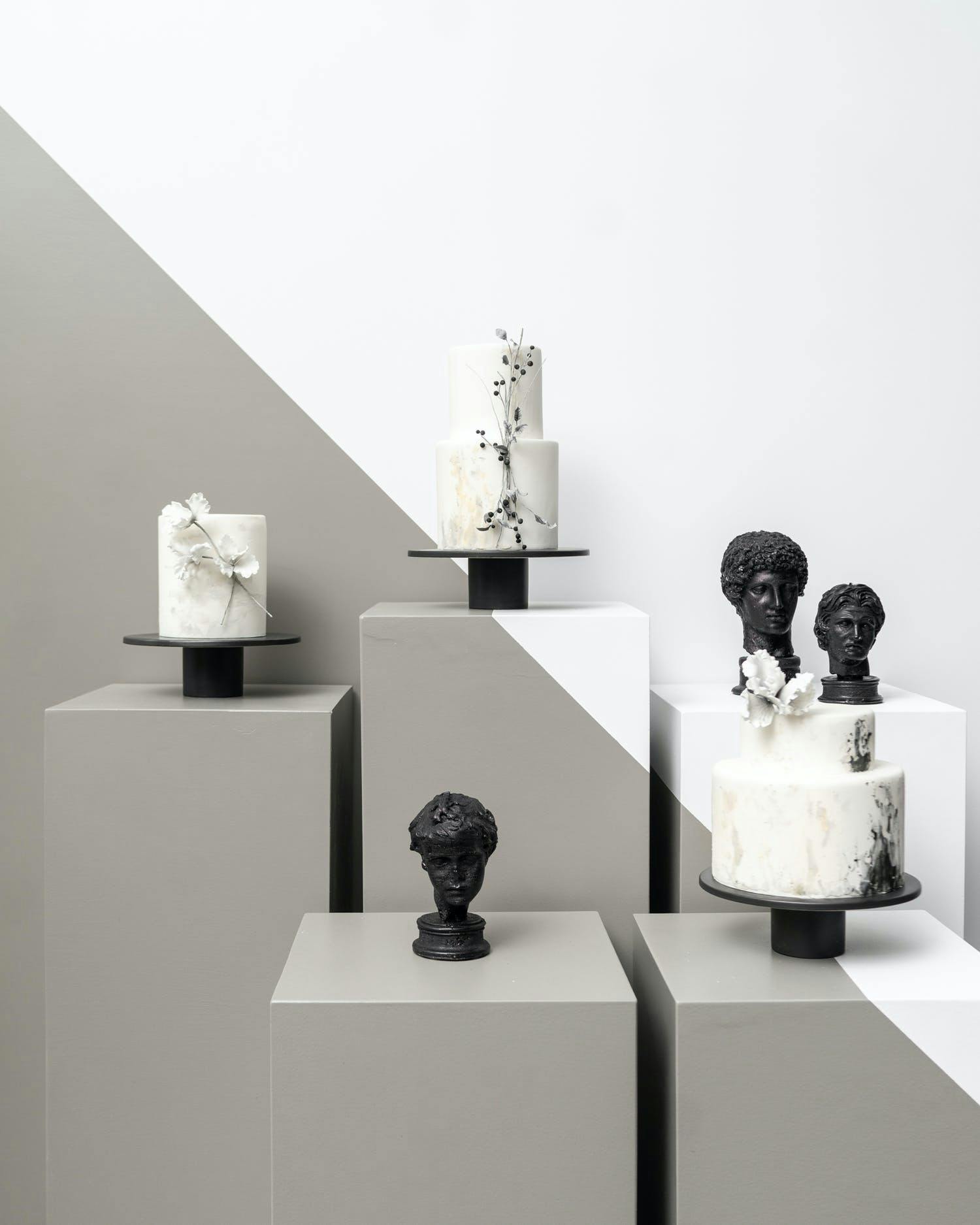 Three Black and White Wedding Cakes with on Gallery-Like Display With Black Statue Heads | PartySlate