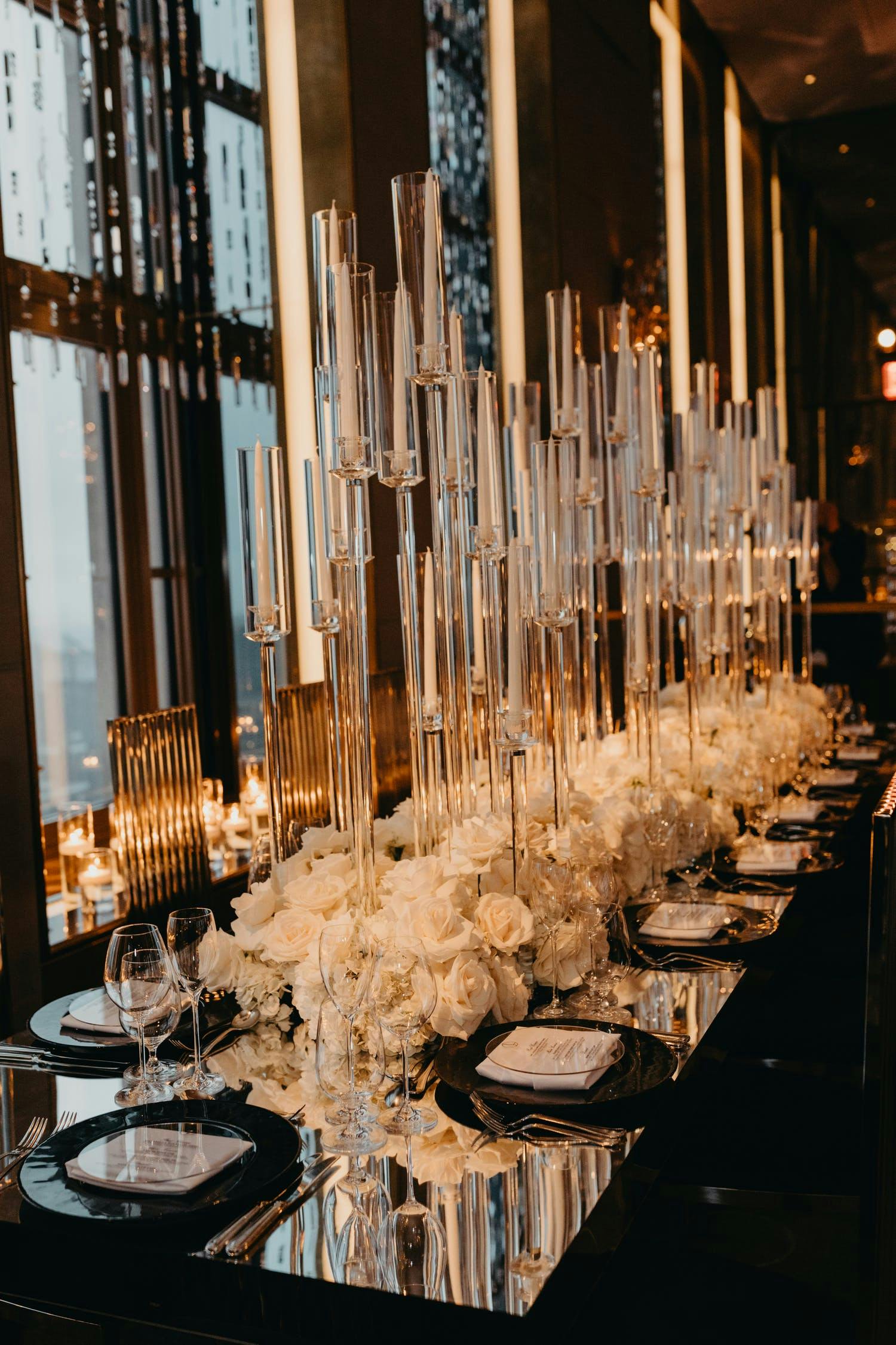 Black and White Wedding Tablescape With Towering Candles, Mirrored Tabletops, White Rose Centerpieces, and Black Dinnerware | PartySlate