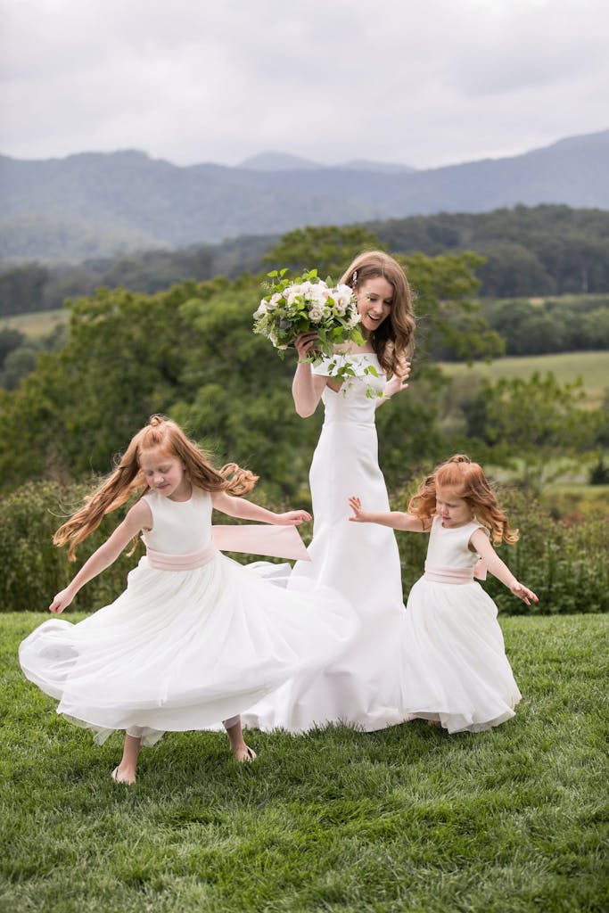 Bride Spins With Two Flower Girls on Hilltop | PartySlate
