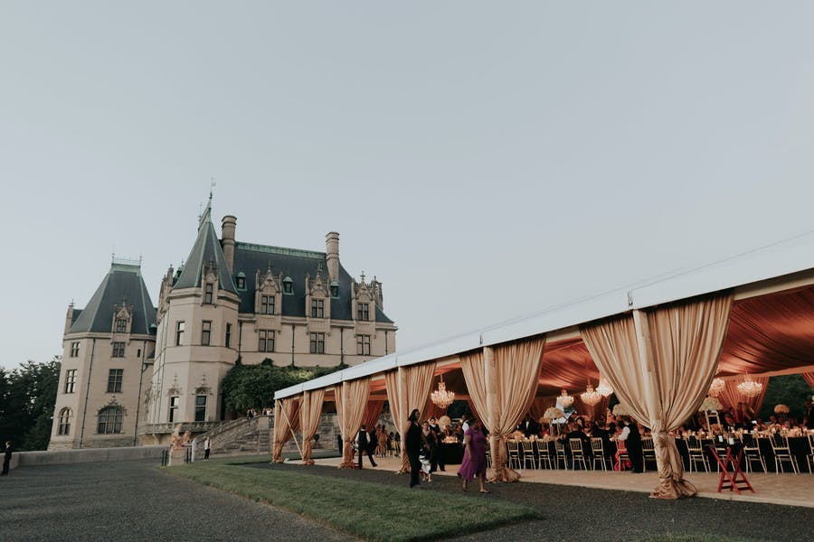 Gold wedding tent next to castle like building | PartySlate