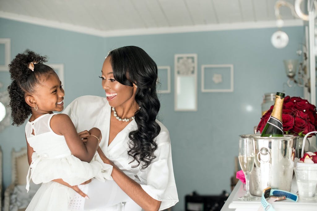 Bride Holds Smiling Flower Girl in Wedding Suite | PartySlate