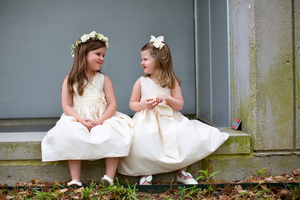 Two Flower Girls Smile at Each Other | PartySlate
