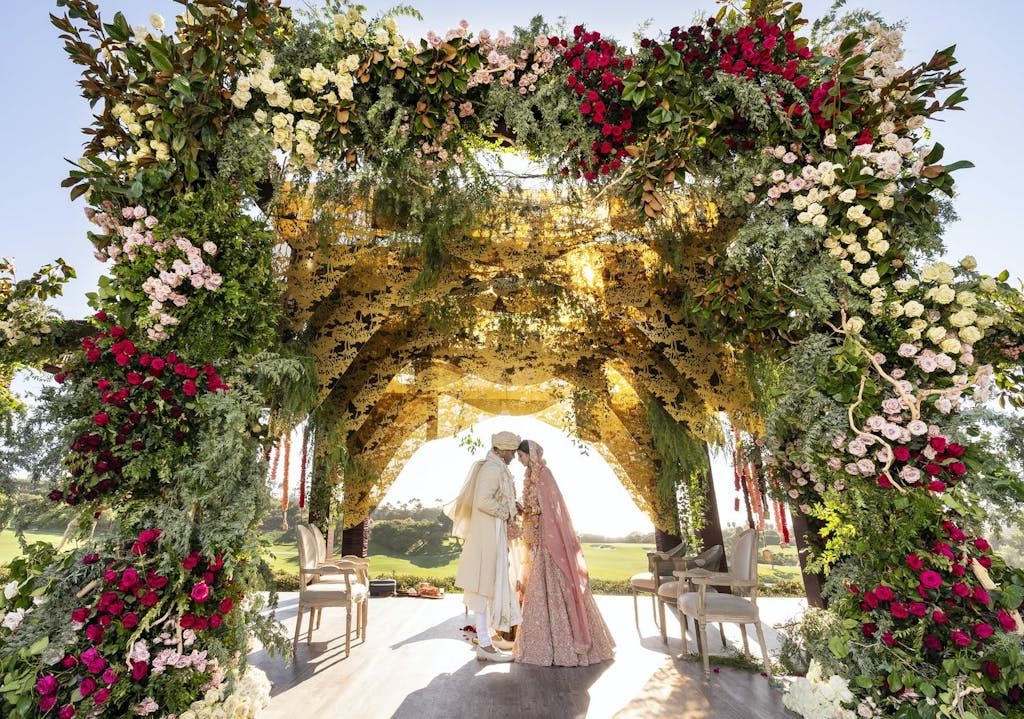 Bride and Groom Touch Foreheads Under a Lavish Floral Mandap | PartySlate