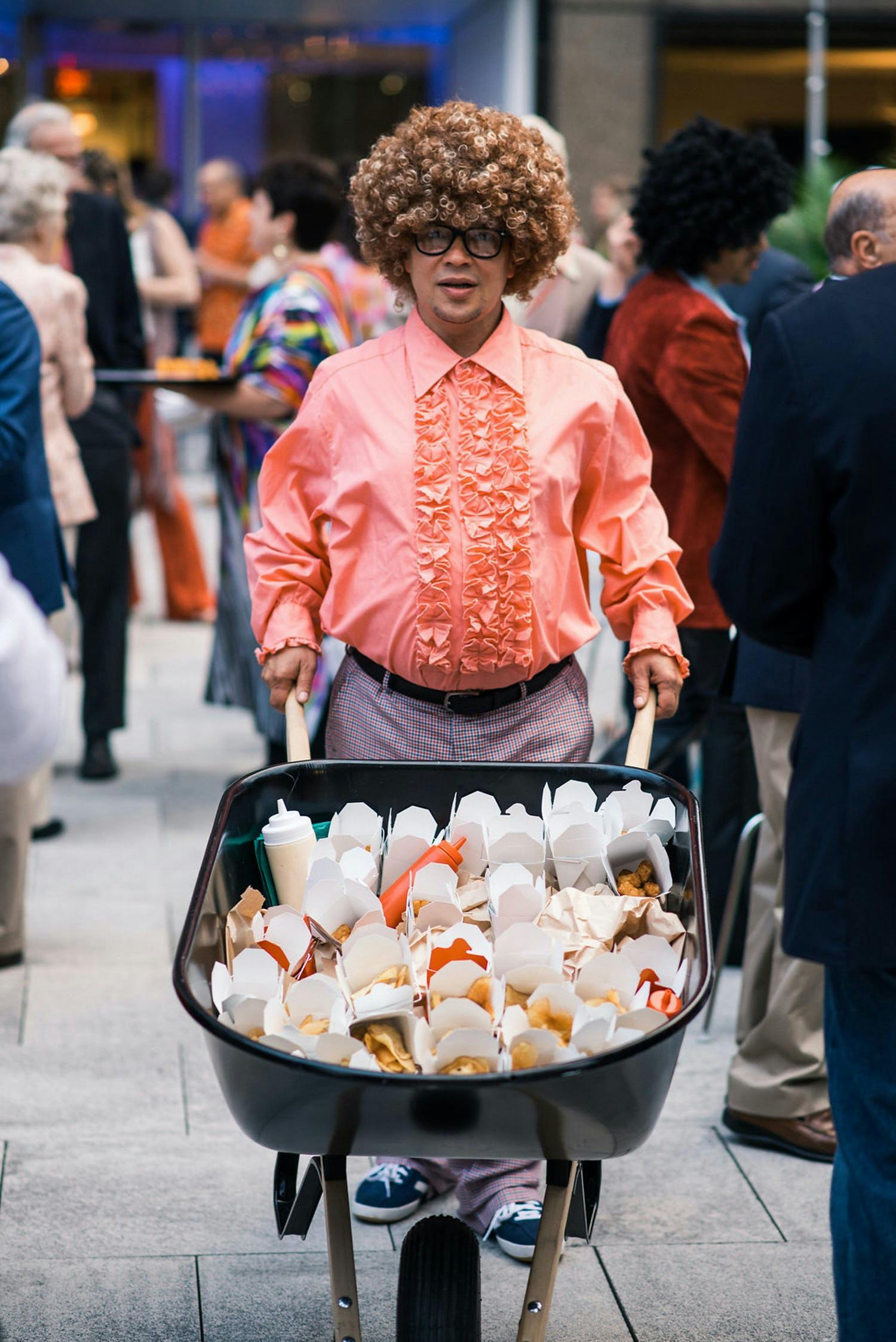 1970'S CALIFORNIA POOLSIDE-THEMED ANNIVERSARY PARTY With Man in Salmon-Color Ruffled Shirt Pushing Wheel Barrow Filled With Ramen Catering | PartySlate