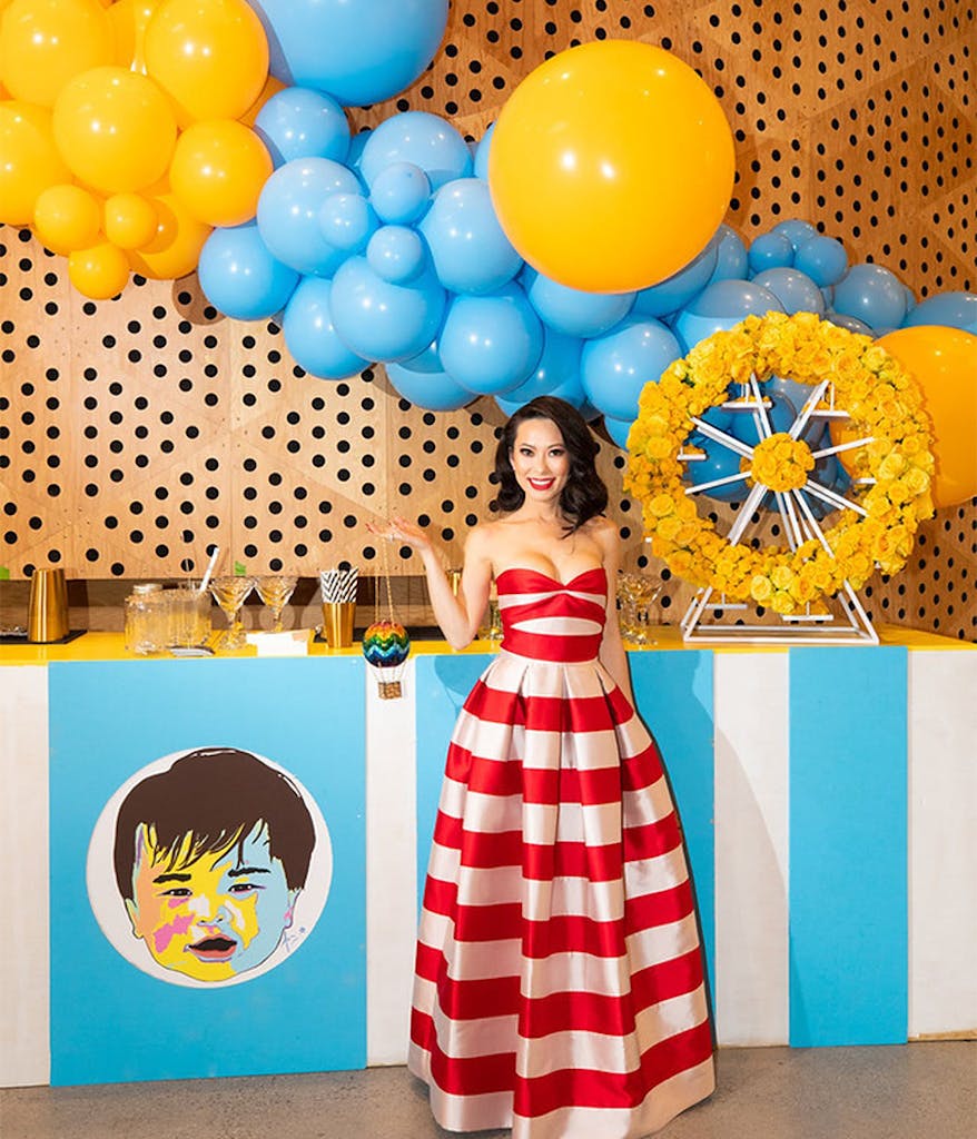 mom at her son's first birthday party wearing a red and white striped dress with yellow and blue balloons