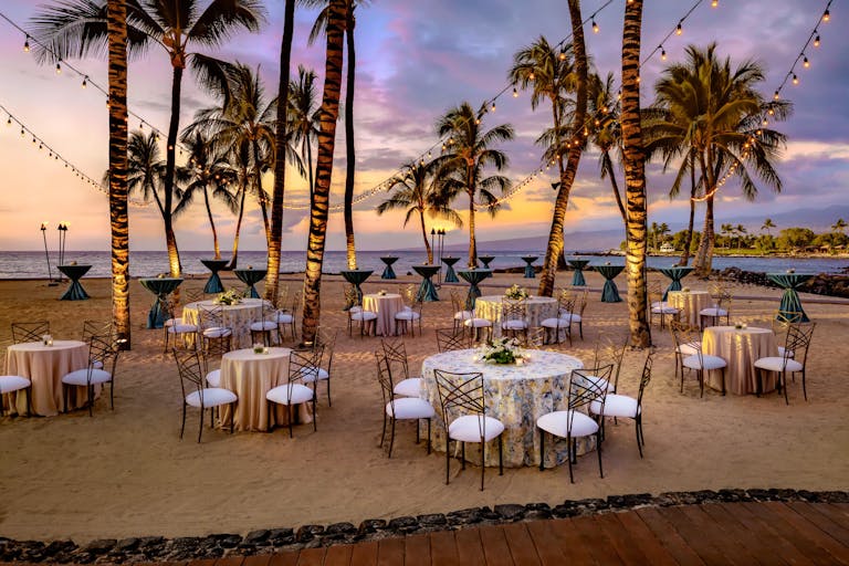 Wedding reception set in sand under palm trees | PartySlate