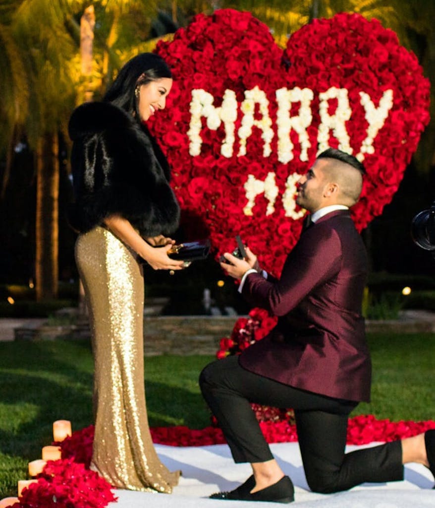 man proposing to his girlfriend outside in front of a heart made out of roses