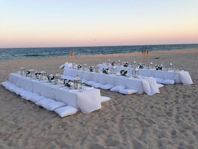 Beach wedding dinner with white linens and white cushions | PartySlate