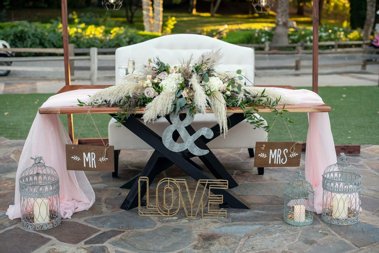 Sweetheart Table With Rustic Wedding Centerpieces Featuring Pampas Grass and Pink Drapery | PartySlate