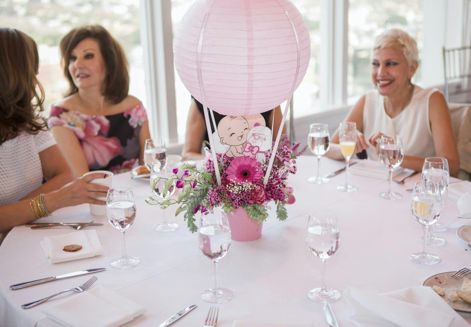 Four Women Sit Around a Table at a Baby Shower With Pink Hot Air Balloon Centerpiece | PartySlate