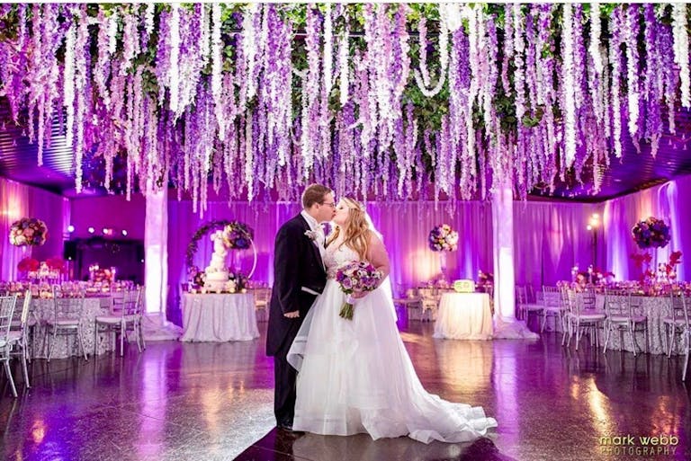 Couple Kiss Under Purple Floral Wedding Ceiling Installation Designed by The Style Marc | PartySlate