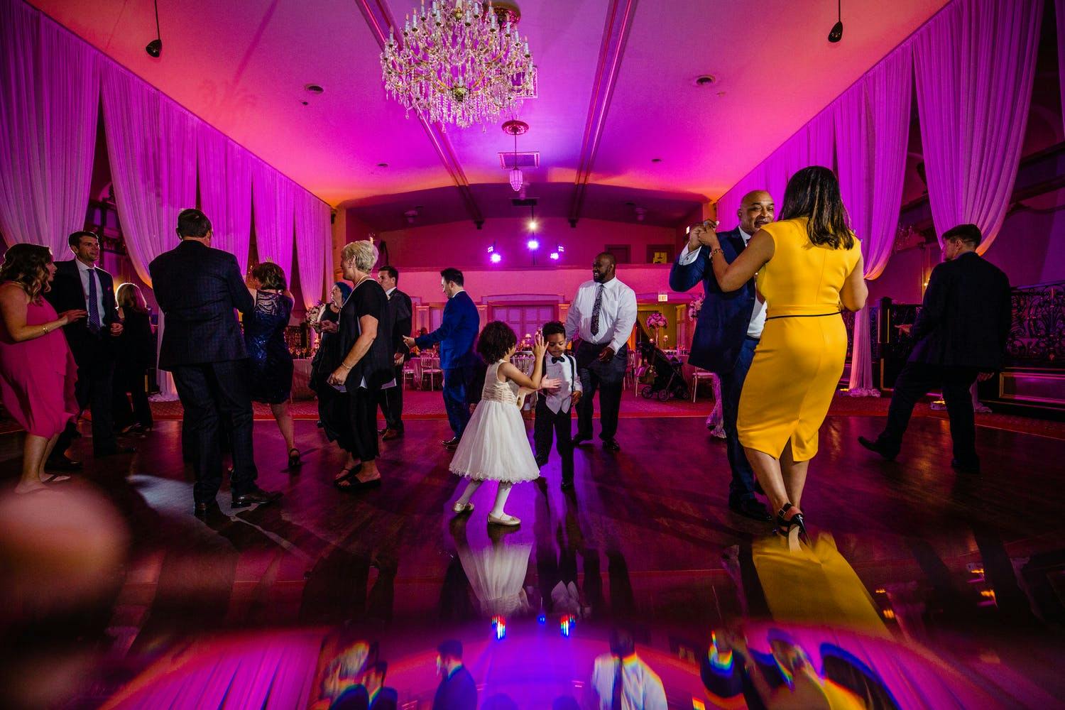 Friend and Family Dance on Mirrored Wedding Dance Floor Amidst Hot Pink Uplighting | PartySlate