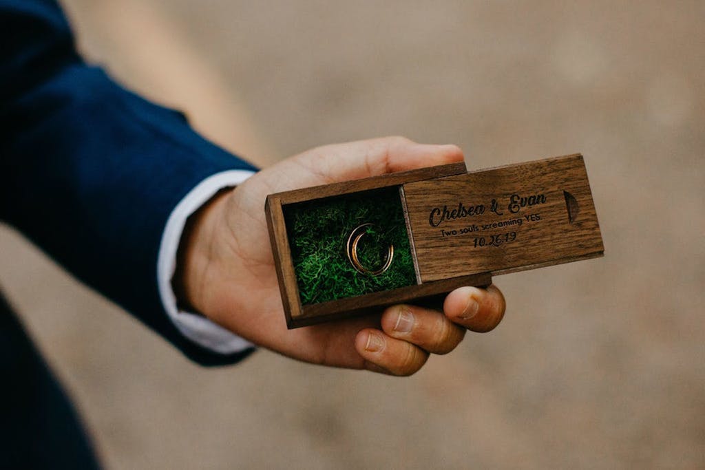 Man in Blue Tux Hold Wedding Ring in Wooden Engraved Box with Bed of Moss | PartySlate