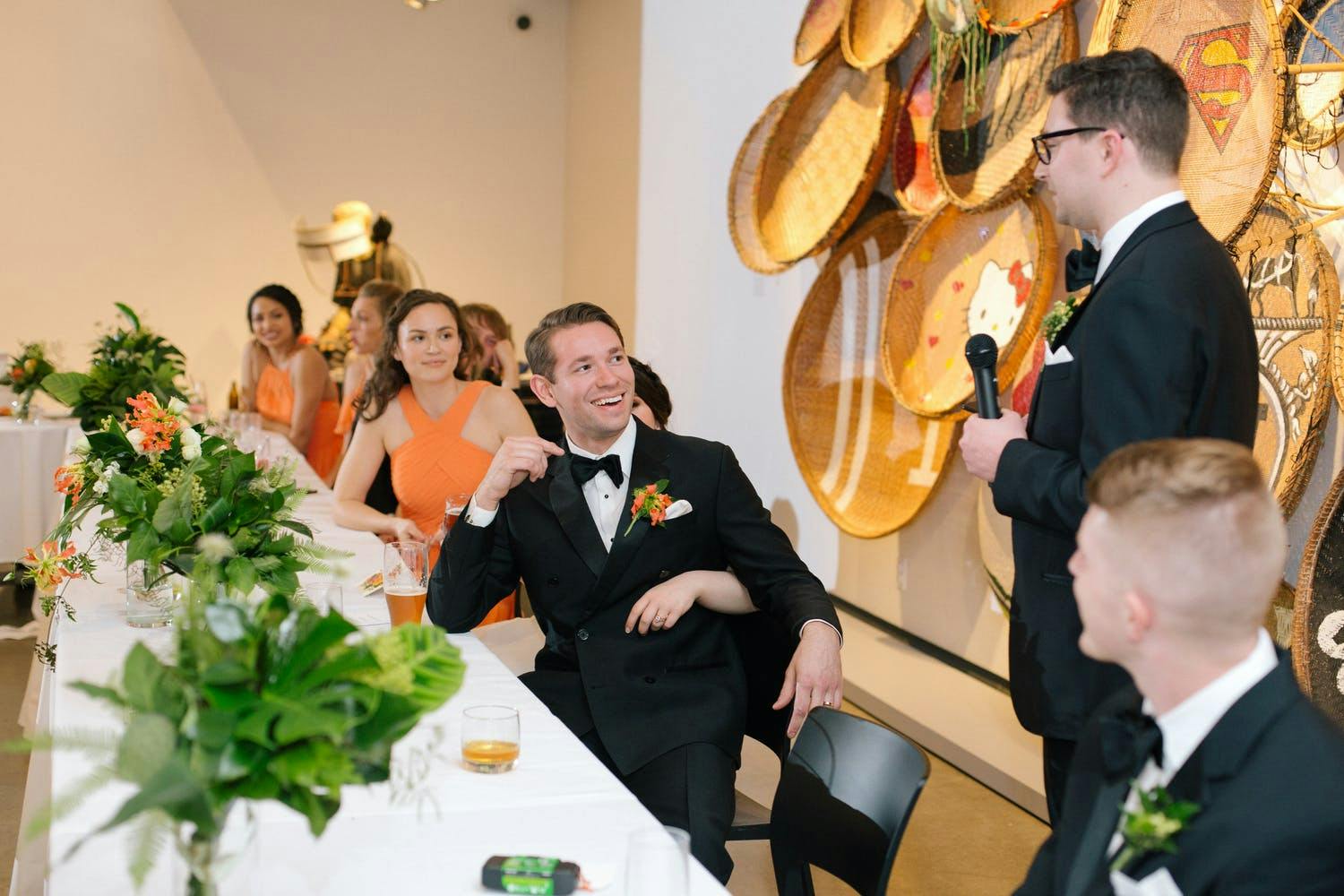 Wedding Party Reception Table at Contemporary Museum. Bridesmaids Wear Orange to Match the Orange-Accented Greenery Centerpieces | PartySlate