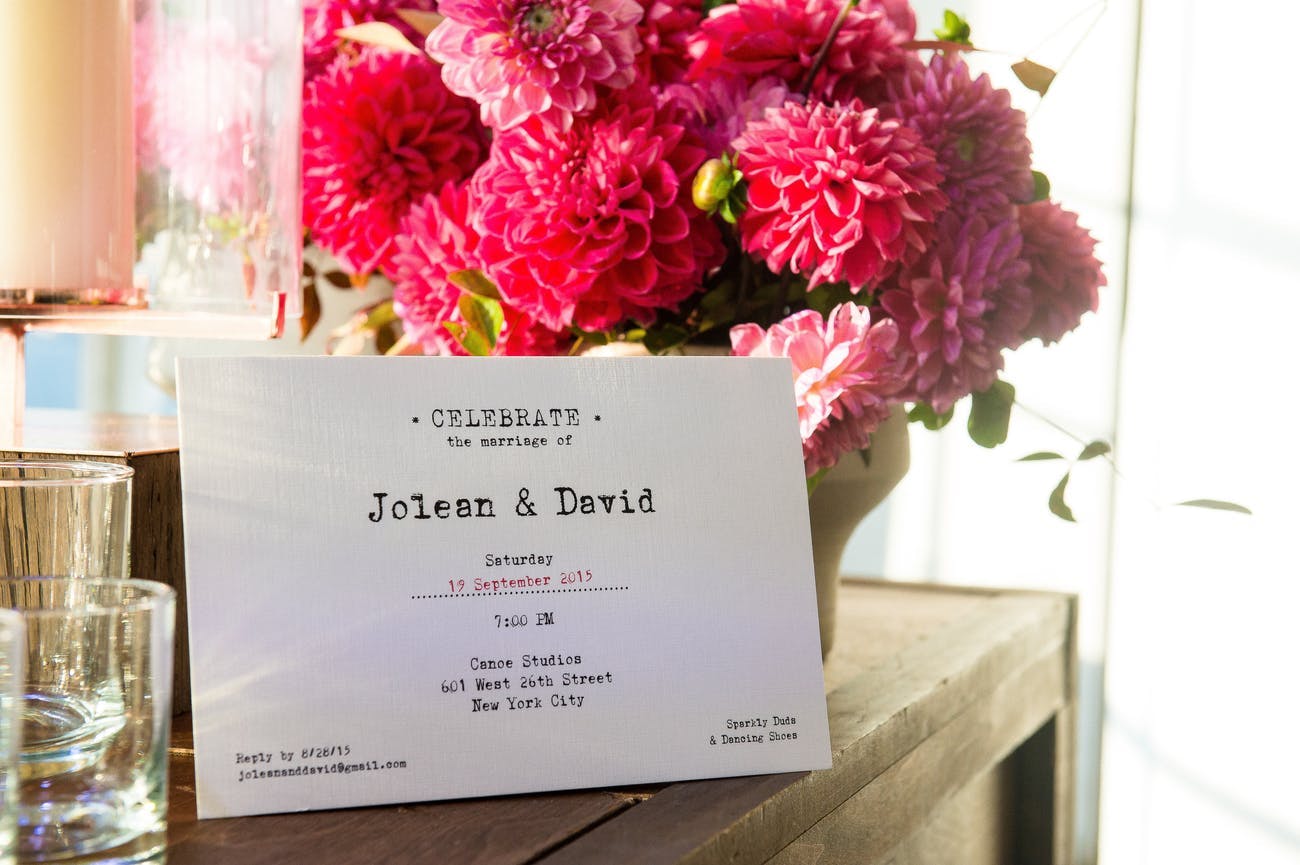 Wedding Invite With Vintage Typewriter Font Against Pink Flower Centerpiece | PartySlate