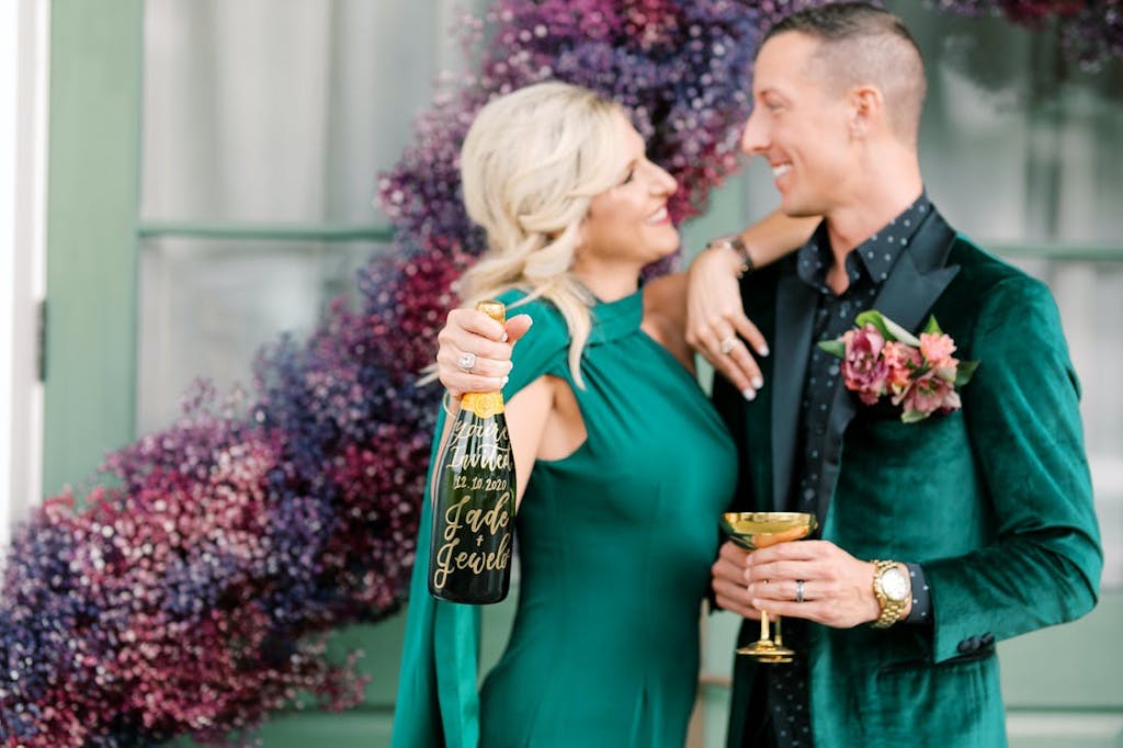 A man and a women in matching emerald green outfits holding a bottle of champagne.