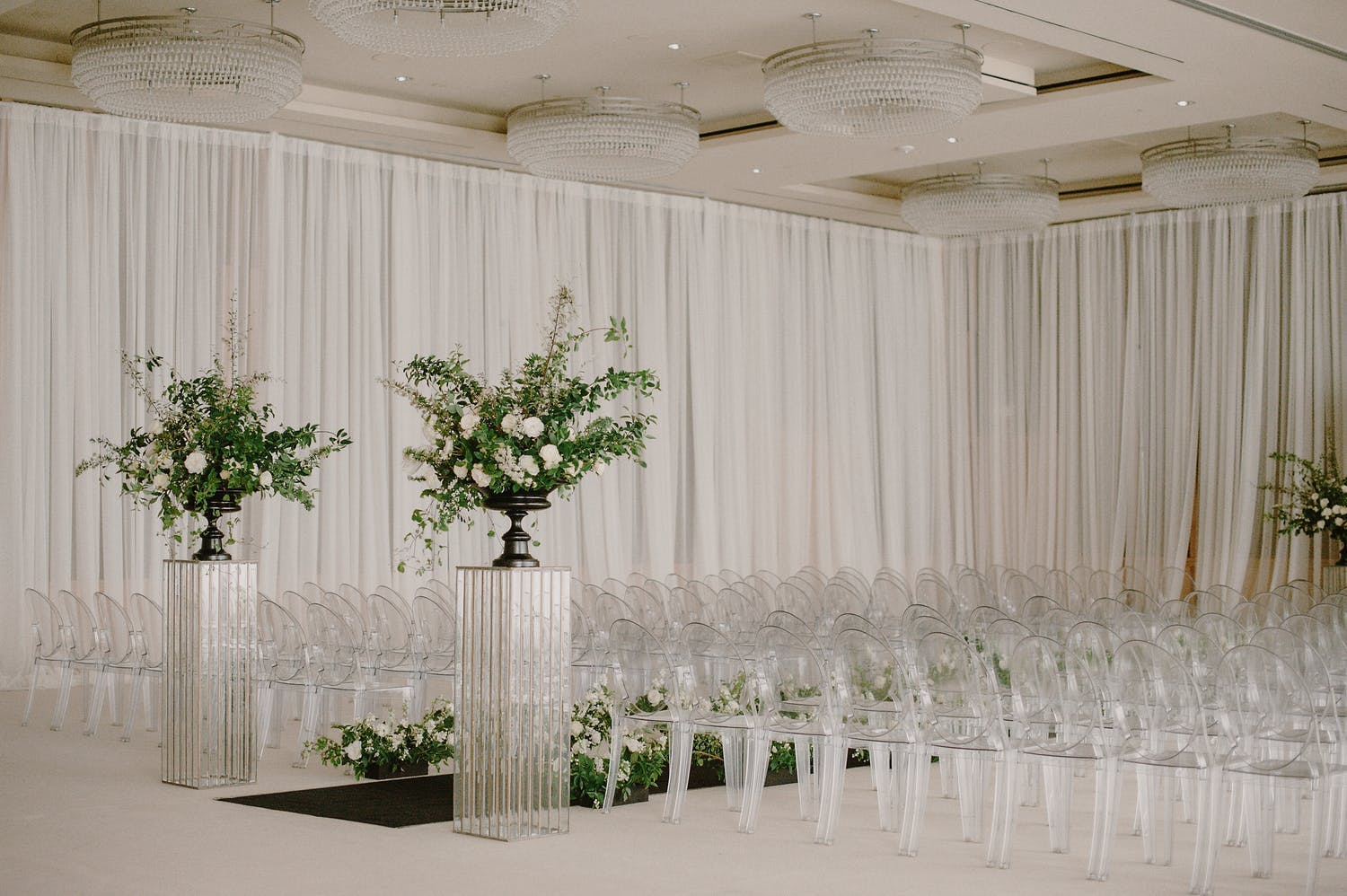 Monochromatic Light Gray Ceremony With Modern Wedding Décor Elements Like Lucite Floral Stands, Gray Drapery, and Ghost Chairs | PartySlate