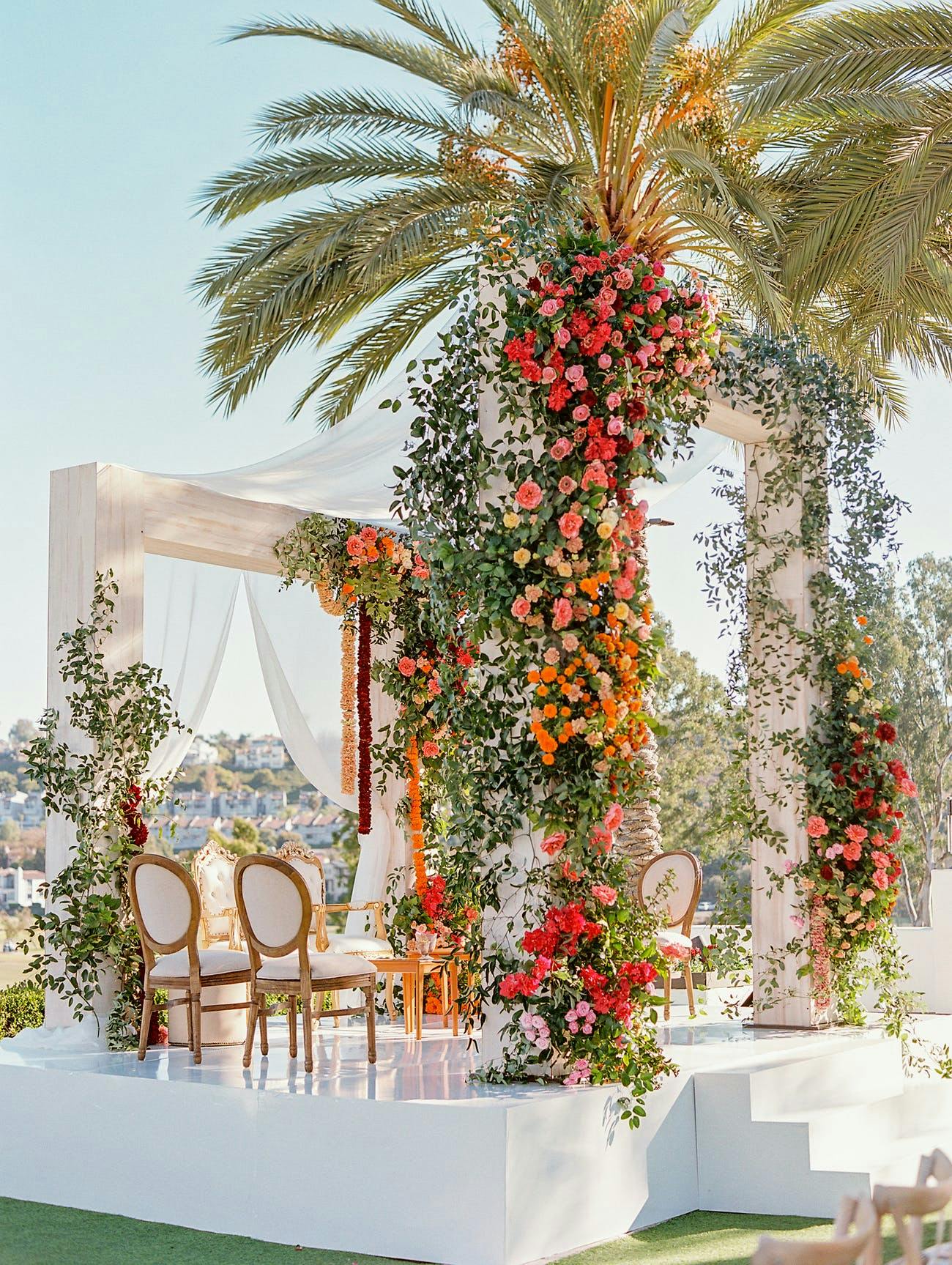Wedding all-white stage with florals wrapped around palm trees | PartySlate