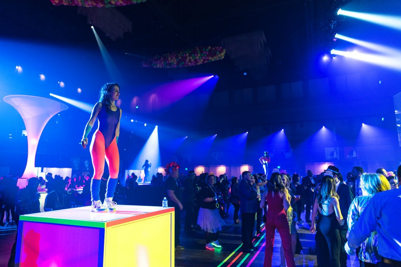 80s Themed New Years Even Party With Vibrant Blue Uplighting and Small Neon Cubed Stage | PartySlate