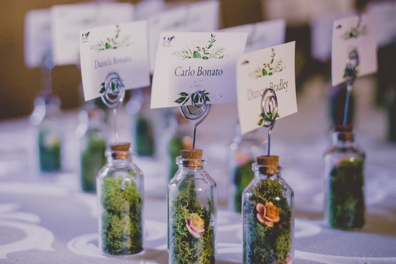 Wedding Escort Cards Attached to Miniature Bottles Filled With Moss and Tiny Flowers | PartySlate