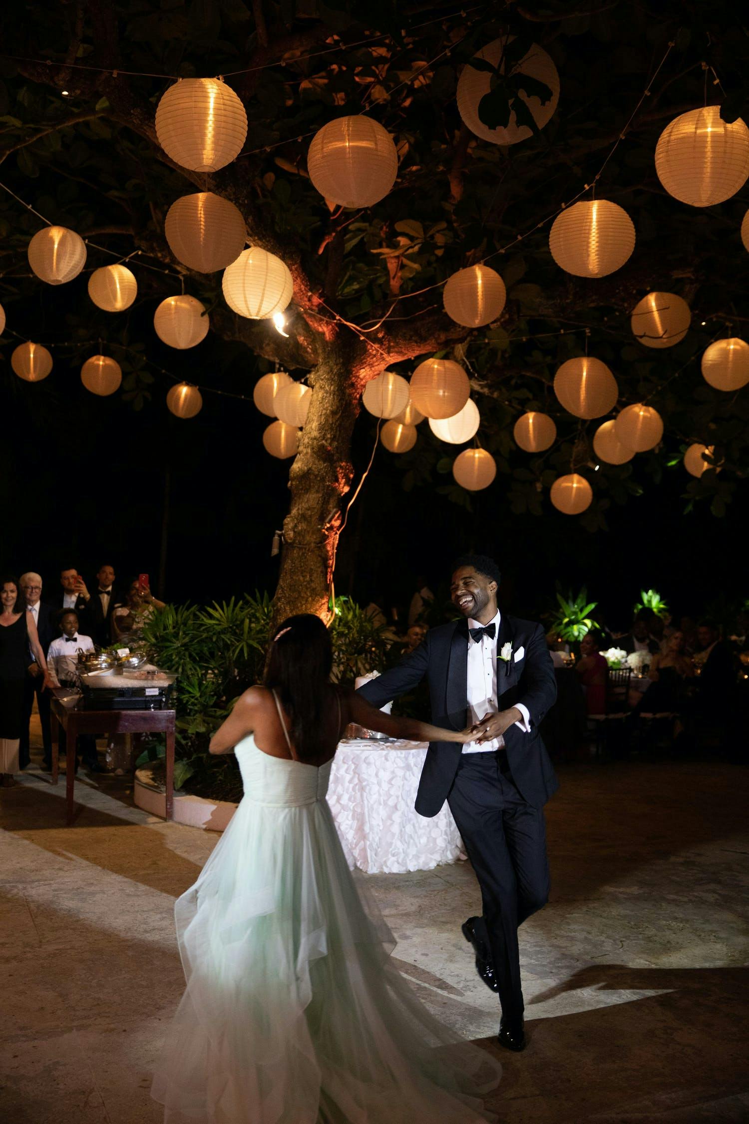 Bride and Groom Dance in Front of a Tree Laden With Globed Paper Lanterns | PartySlate