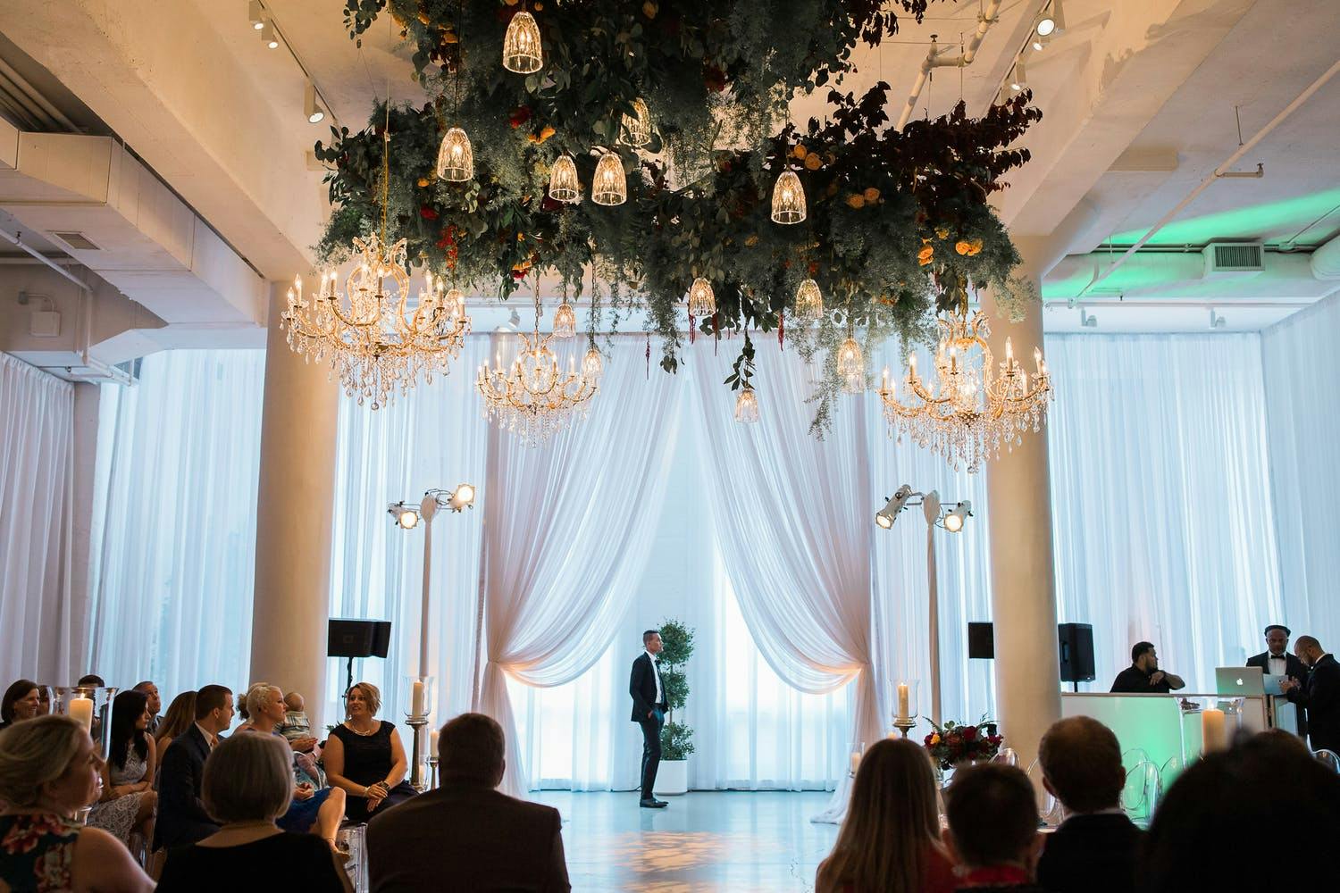 White Wedding Ceremony With Pillars, Sheer Draper, and Ceiling Installation of Greenery and Lighting | PartySlate