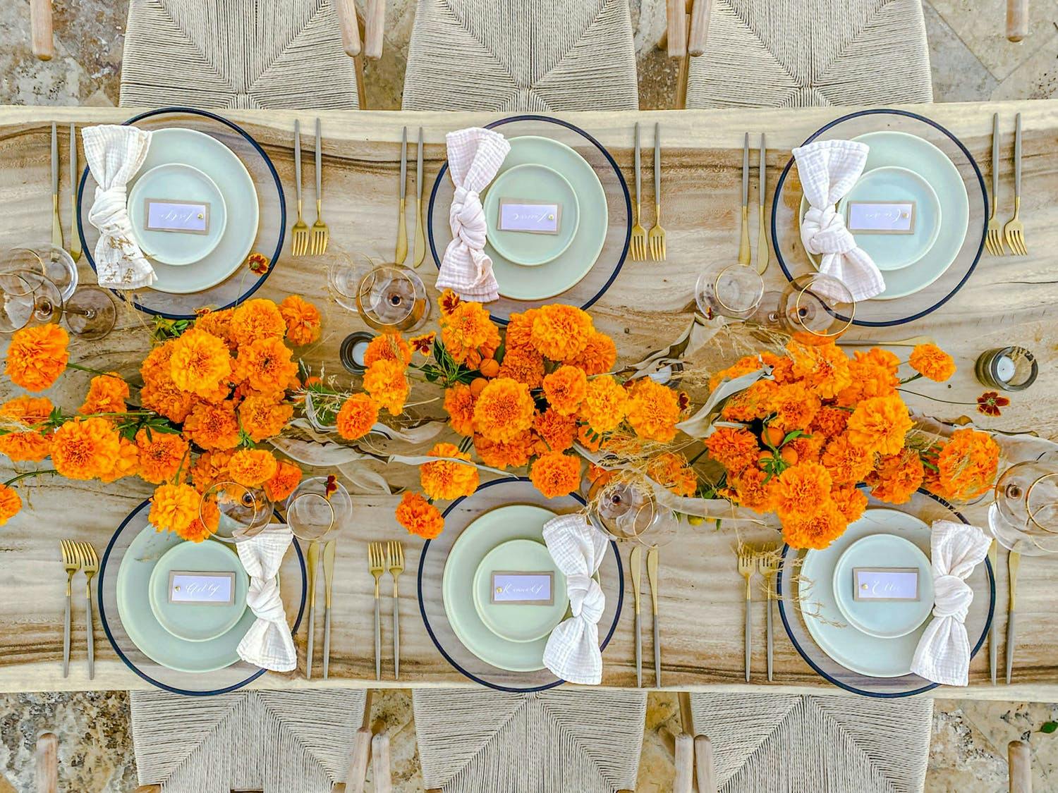 Wooden Table With Orange Wild Flowers and Pale Green Dishware | PartySlate