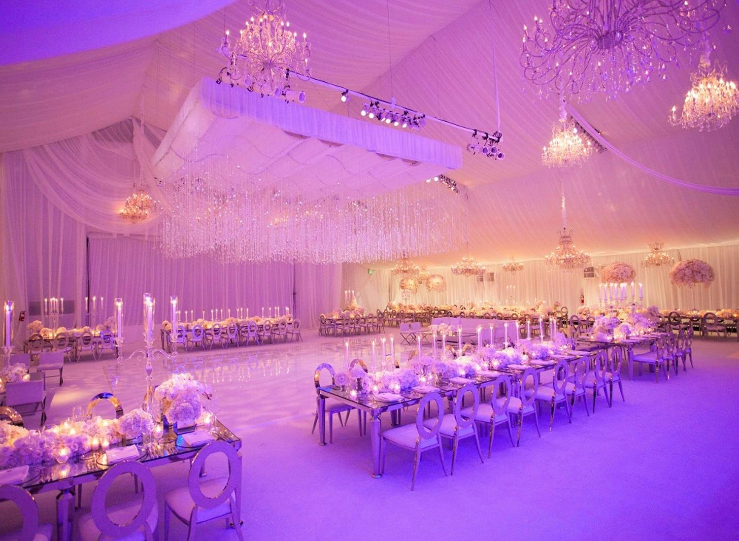 Tented Wedding with Suspended Crystal Ceiling Décor, Pink and Purple Uplighting, Polished Dance Floor, and Long Reception Tables | PartySlate