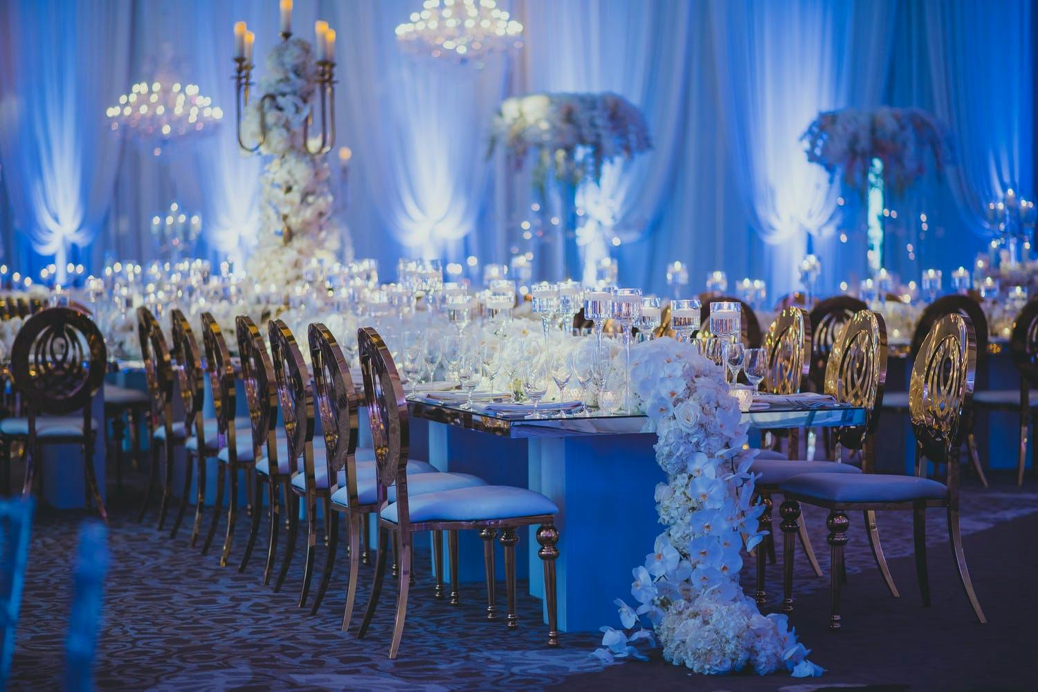 Wedding Reception With Orchid Garland Centerpiece, Gold Seating, and Blue Uplighting | PartySlate