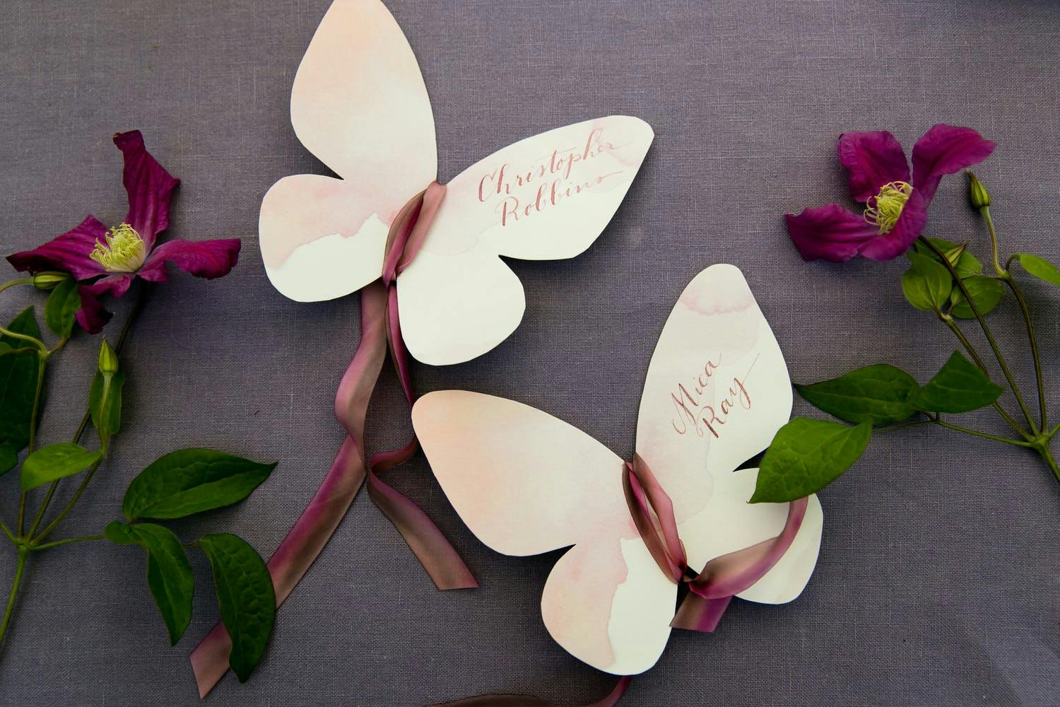 Paper Butterfly Wedding Escort Cards With Mauve Ribbon and Greenery | PartySlate
