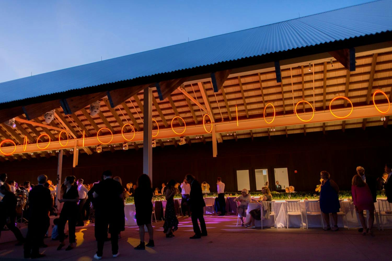 Roofed Wedding Reception Area With Golden Neon Rings Suspended from Ceiling | PartySlate