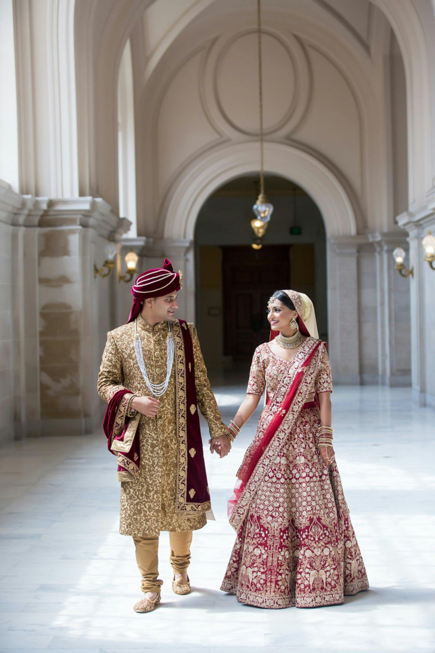 Bride and Groom Walk Down Vaulted Hallway at South Asian Wedding | PartySlate