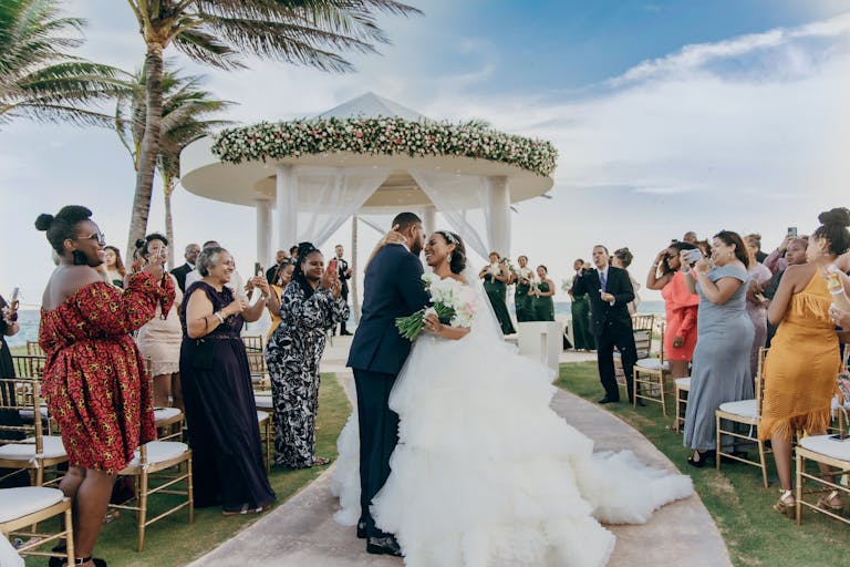 Bride and Groom Kiss During Recessional Walk With Floral-Wrapped Circular White Arbor in Background | PartySlate
