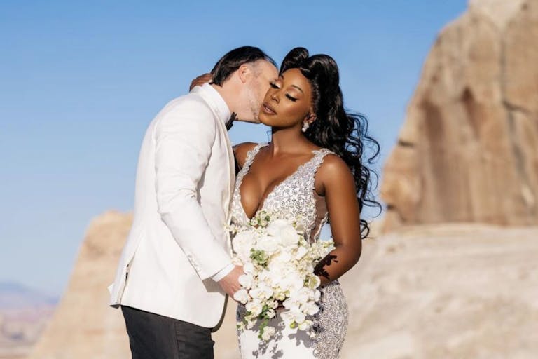 Groom Kisses Bride Against Desert Backdrop With Deep Blue Sky | PartySlate