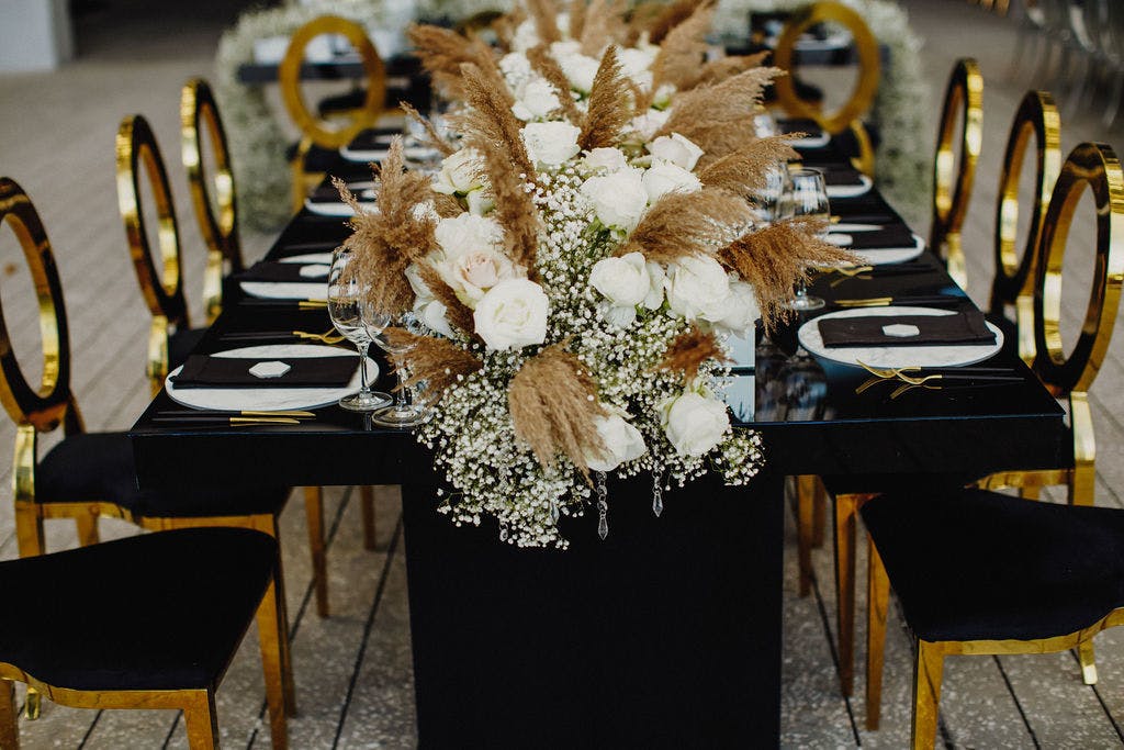 Black Modern Tablescapes with Mirrored Gold Accents and Wedding Centerpieces Featuring Garland of Baby’s Breath, Pampas Grass, and White Roses | PartySlate