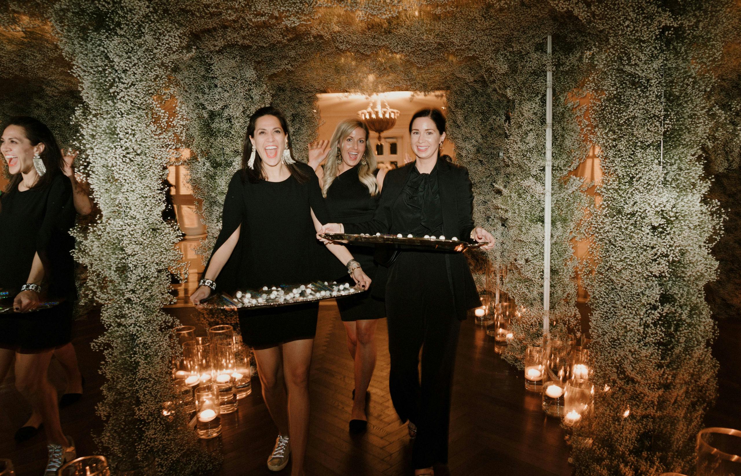 Three Wedding Staff Servers Smile Underneath Wedding Canopy Covered in Baby’s Breath