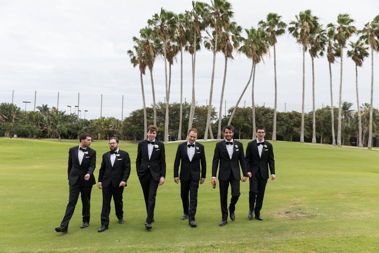 Groom's Party Poses in Front of Green Sprawling Lawn with Palm Trees in Backdrop | PartySlate