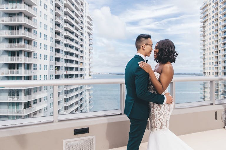 Wedding Photo of Bride and Groom on Balcony Overlooking Skyscraper and Ocean Captured by Stanlo Photography | PartySlate