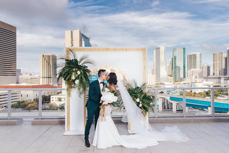 Bride and Groom Kiss In front of Modern Arch at PENTHOUSE at Riverside Wharf Overlooking Skyline | PartySlate