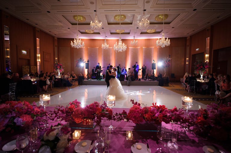 Bride and Groom Dance on White Dance Floor Behind Pink-Floral Tablescapes at Ballroom in The Peninsula Chicago | PartySlate